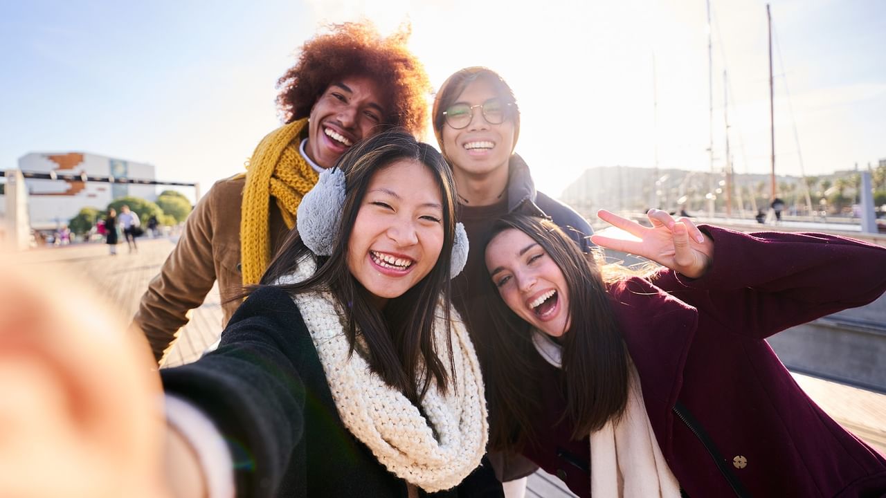 Four friends smiling and taking a selfie together at the waterfront with Midweek Savings in Vancouver.