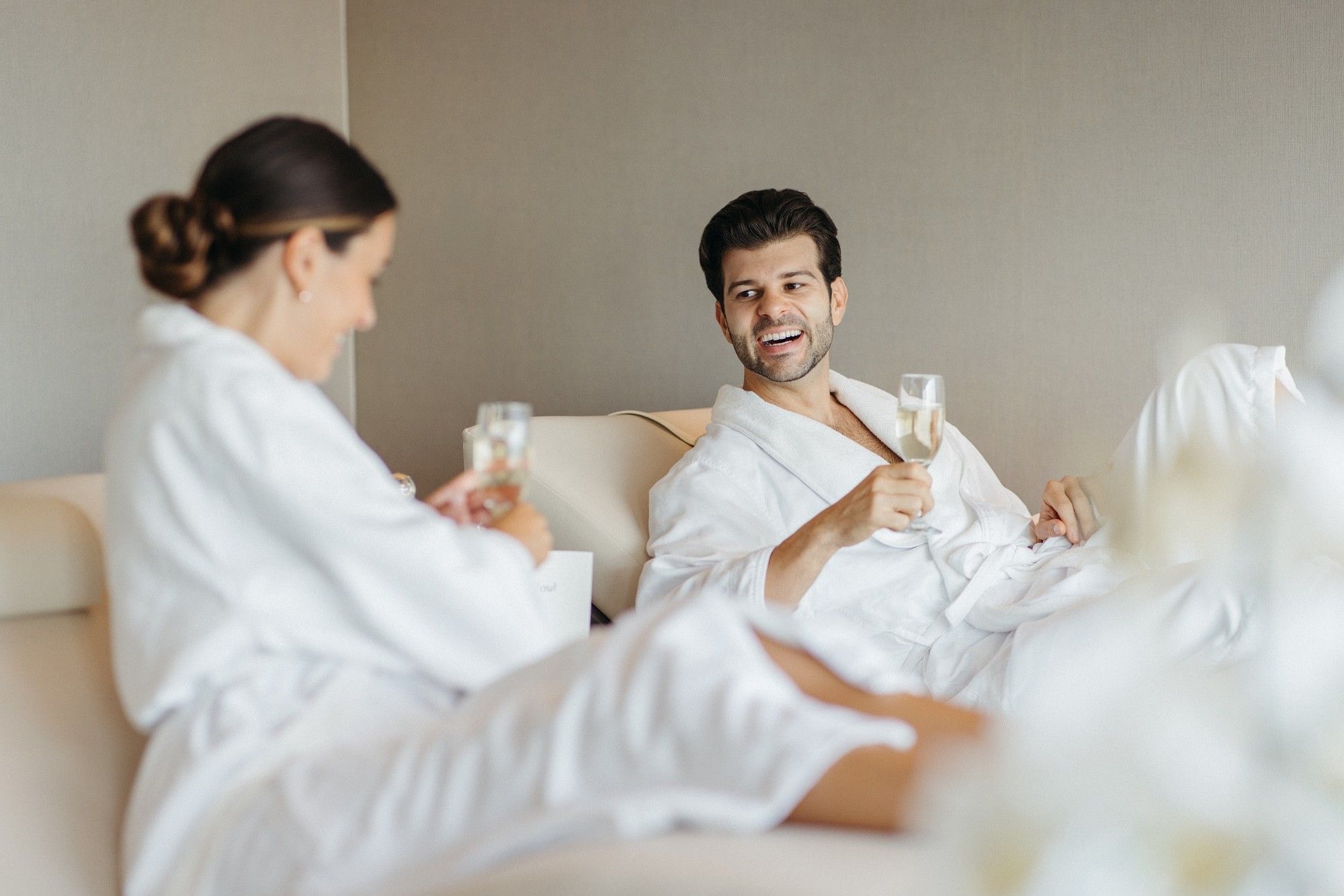 Man and woman in plush white bathrobes relaxing with champagne glasses on lounge chairs at Hotel X Toronto