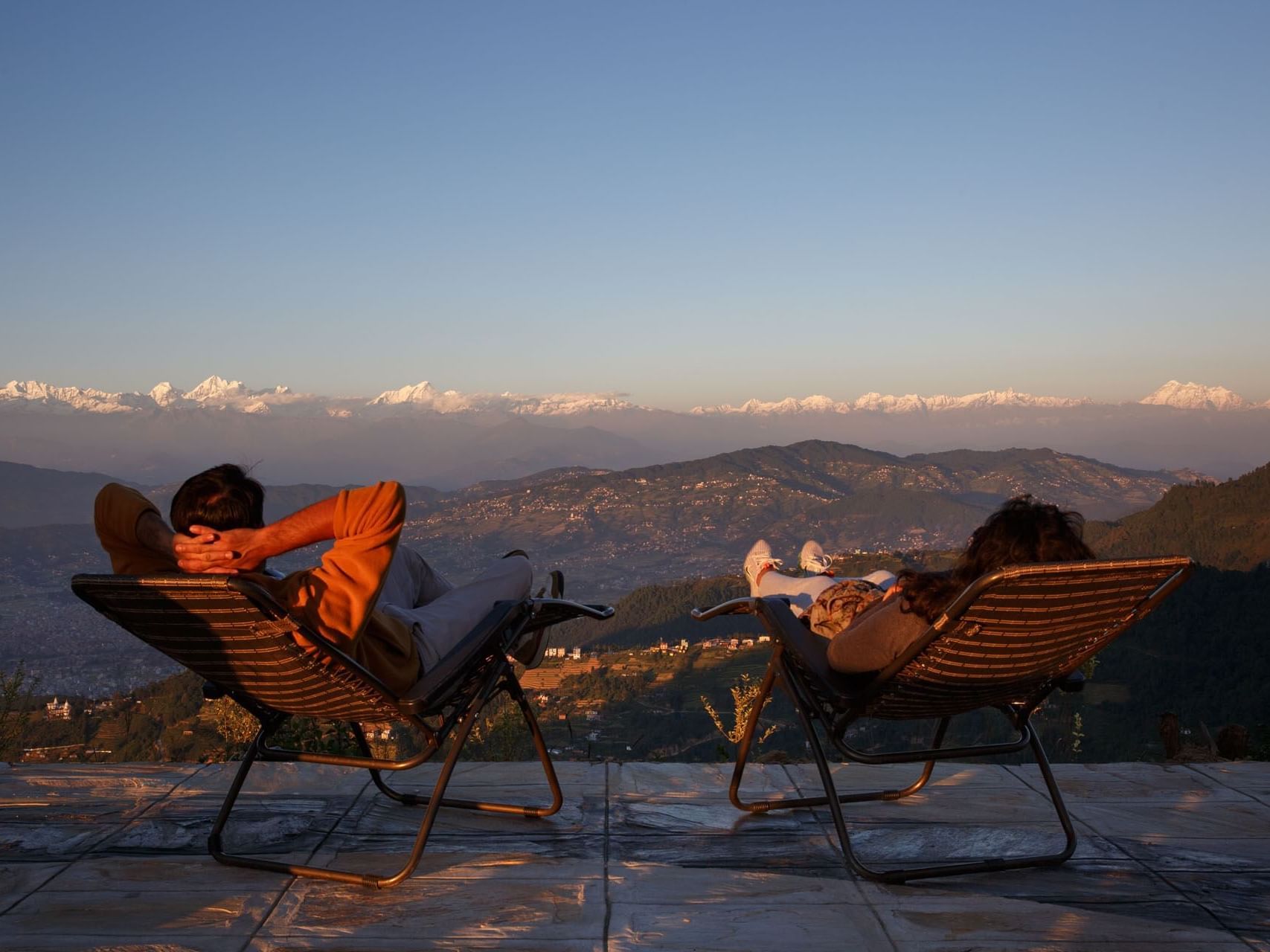 Couple relaxing on chairs against a backdrop of snowy mountains at sunset at The Terraces Resort & Spa