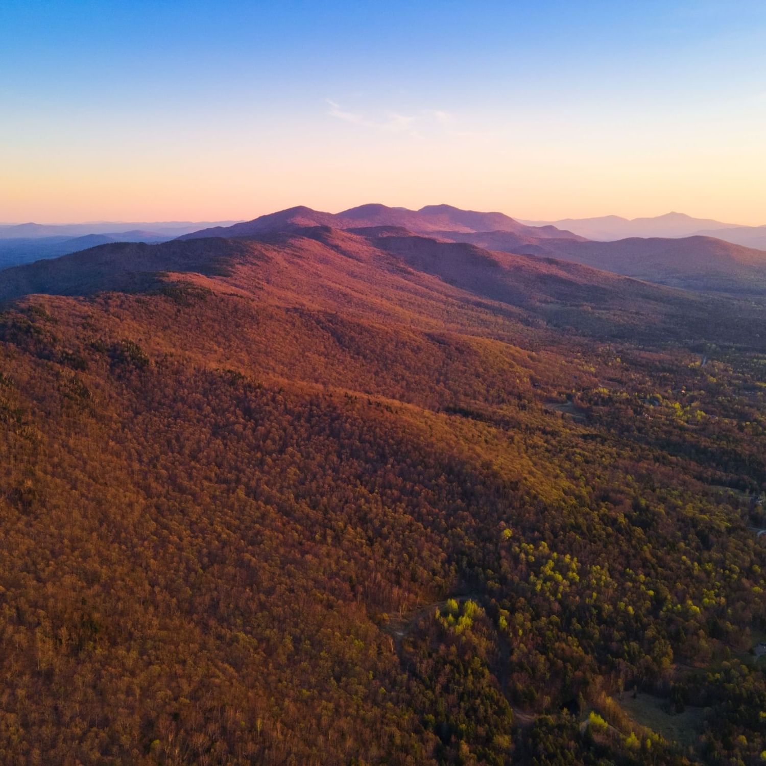 Aerial view of a mountain range with colorful foliage under a clear blue sky.