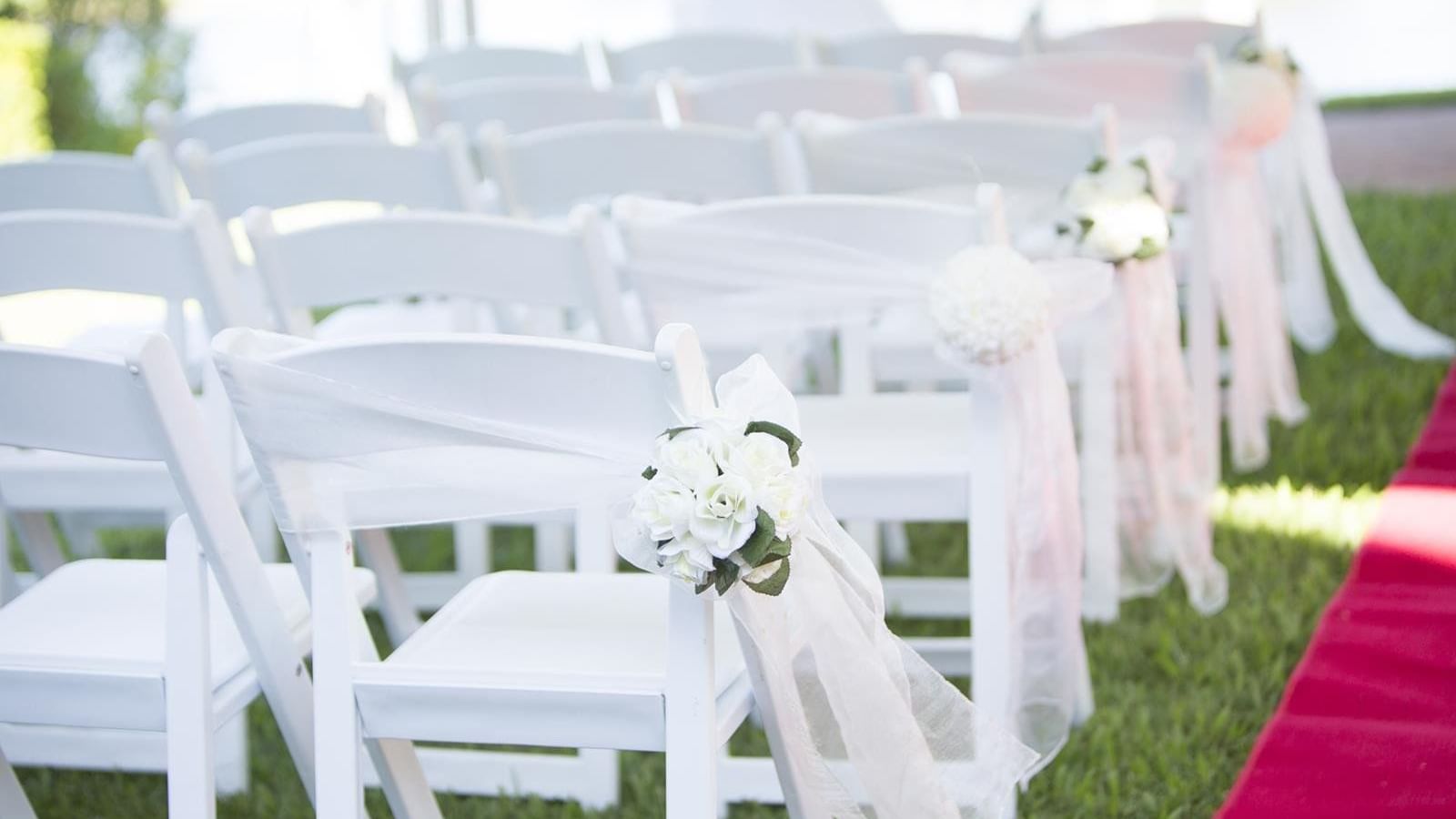 Rows of white chairs with ribbons and florals set outdoors for a wedding ceremony at Mercure Hotel Townsville