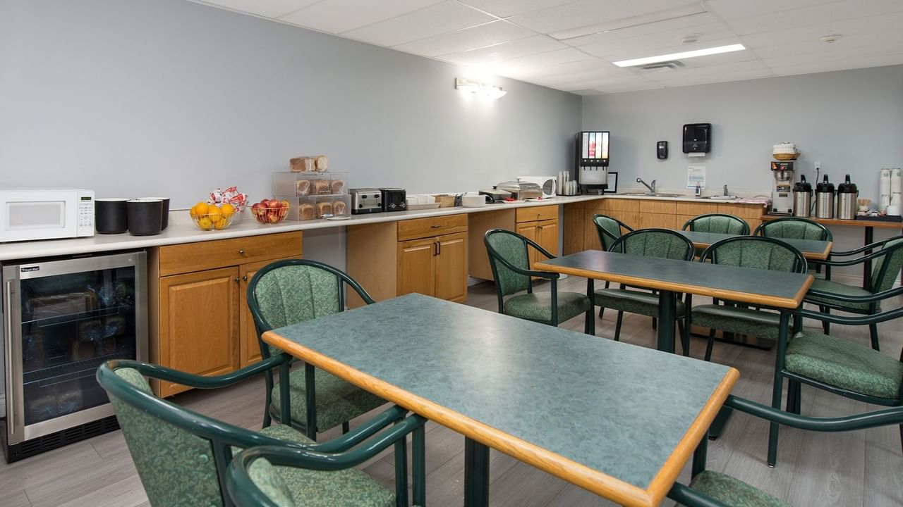 An empty break room with tables, chairs, a microwave, coffee machines, and a cooler.