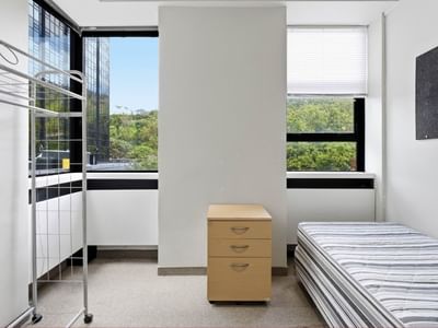 A bedroom with a single bed, wooden drawer, and metal bunk bed frame.