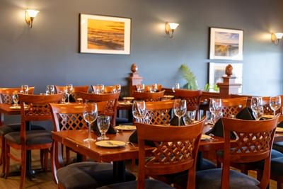 Set dining tables with wine glasses and wooden chairs inside the restaurant at Rodd Crowbush Golf & Beach Resort