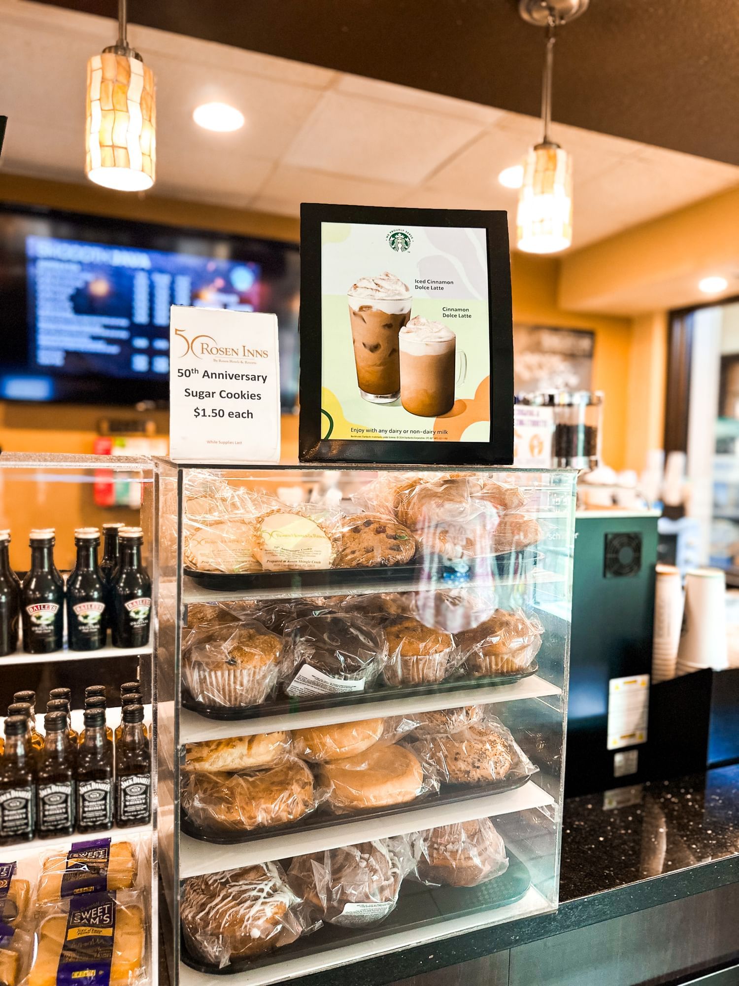 A display case at Rosen Inn at Pointe Orlando's Smoooth Java features pastries and two signs – one advertising 50th Anniversary sugar cookies and the other advertising Starbucks drinks with an image of two coffees.