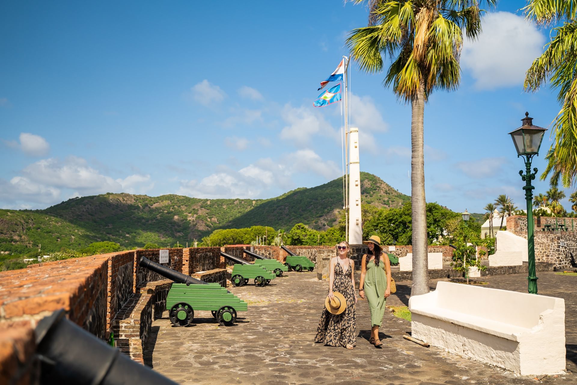 Twee vrouwen die door een historisch fort in Oranje op Sint Eustatius lopen, met kanonnen en palmbomen, Golden Rock Resort