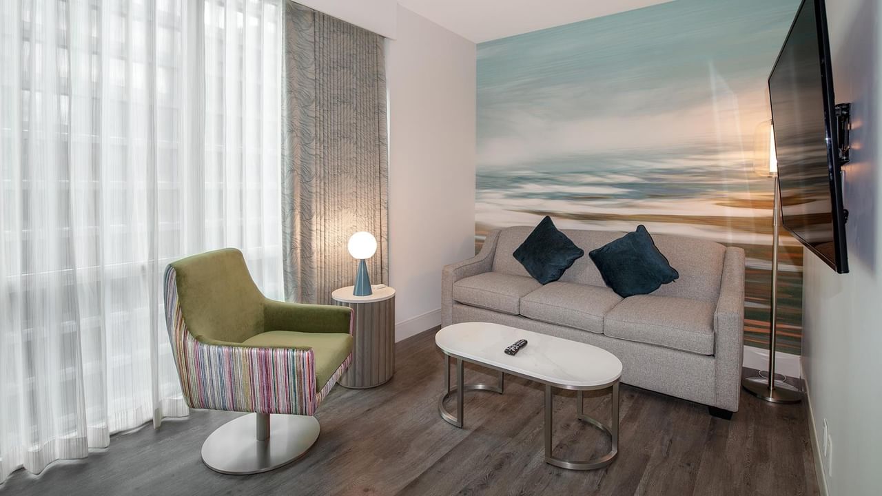 Hotel room with couch, chair, coffee table, and flat screen TV.