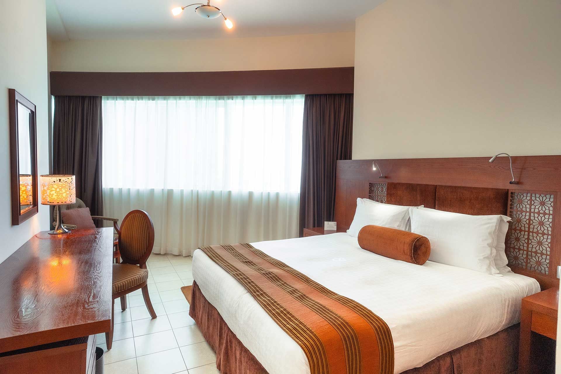 Work desk facing bed by the window and tiled floors in room at Tamani Marina Hotel