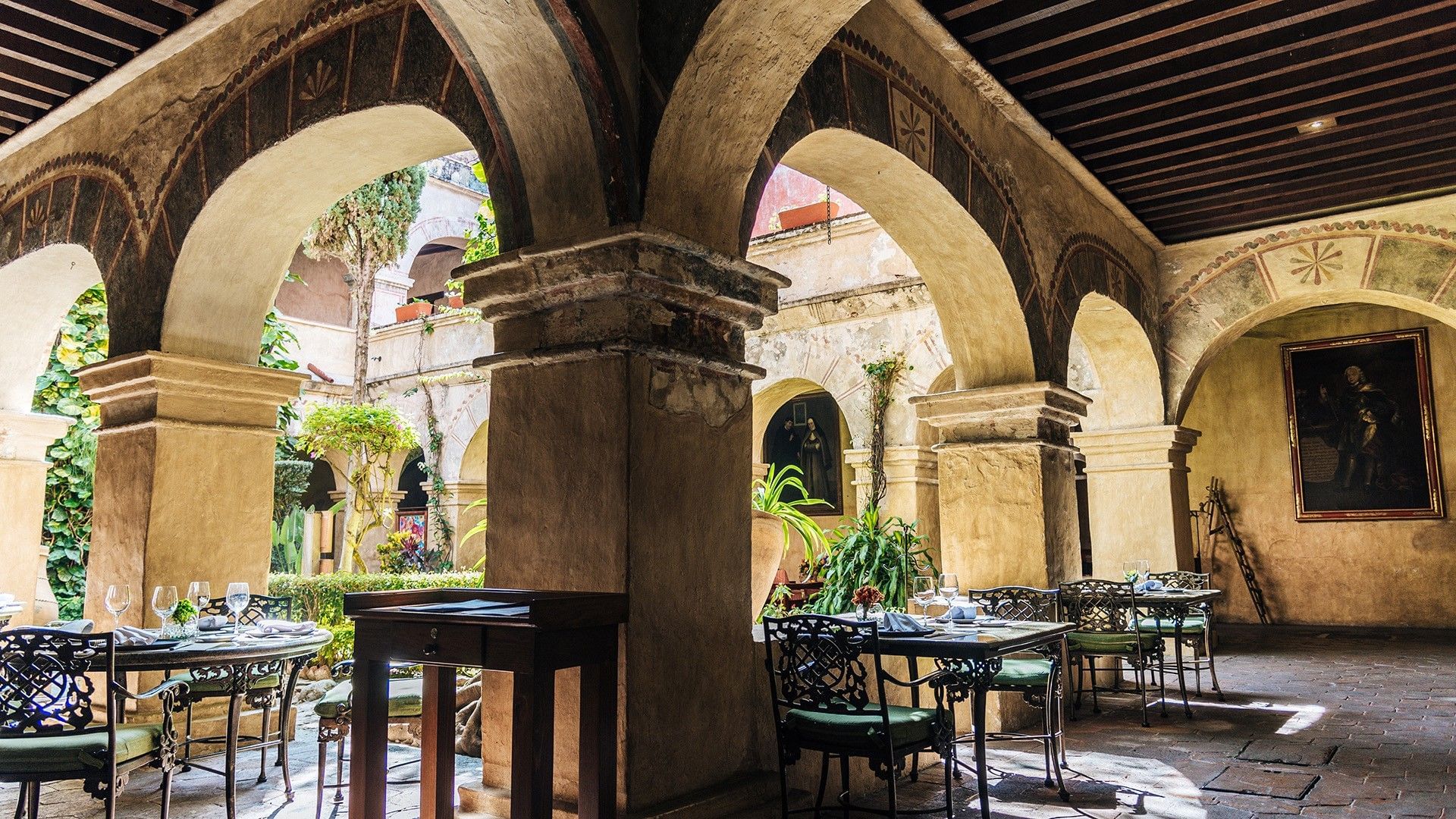 El Refectorio with arched stone columns and ornate metal tables set for dining at Quinta Real Oaxaca
