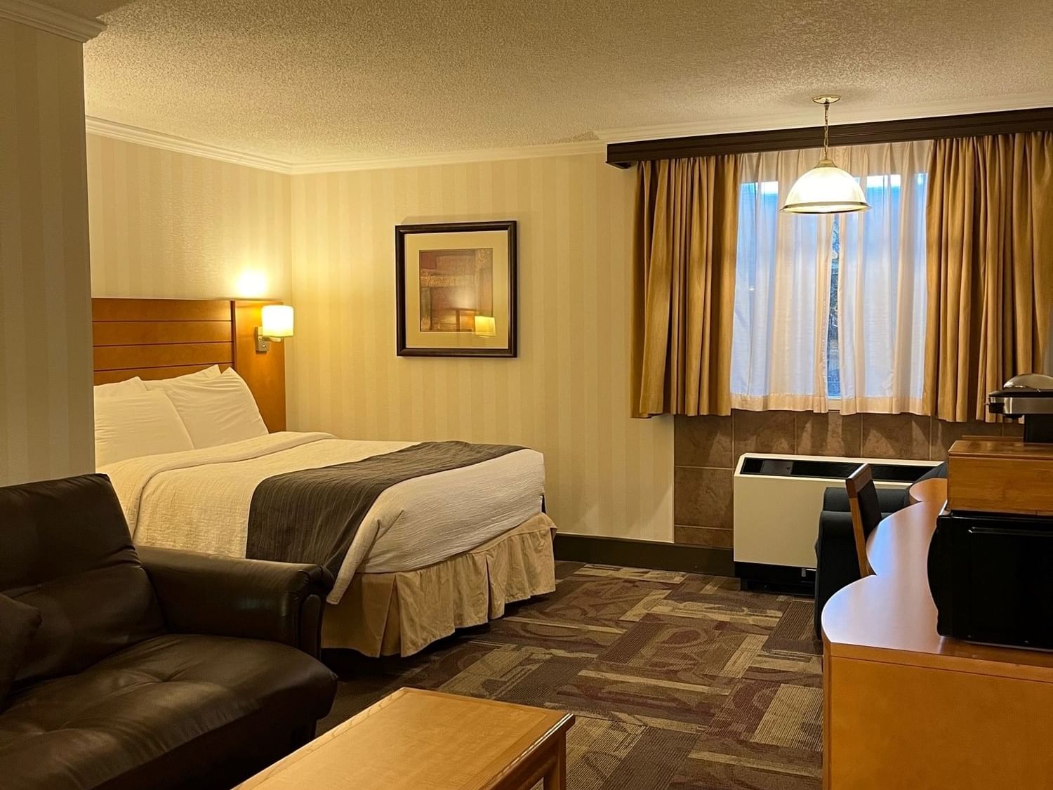 Large bed with sofa and work area in illuminated Queen Bed Standard at The Glenmore Inn & Convention Centre