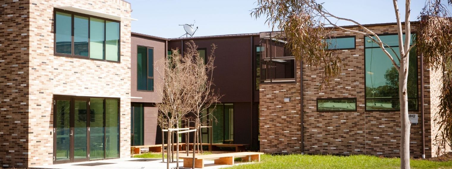 Modern brick building with glass windows, green lawn, and a small outdoor seating area.
