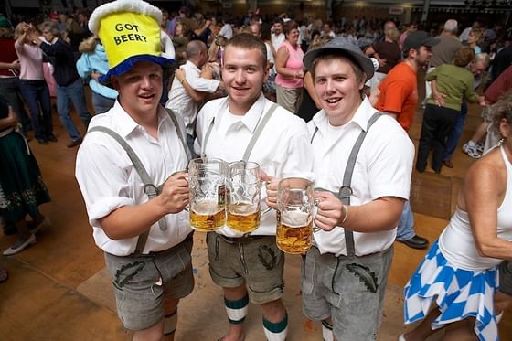 3 people holding beers in October fest near Marv Herzog Hotel