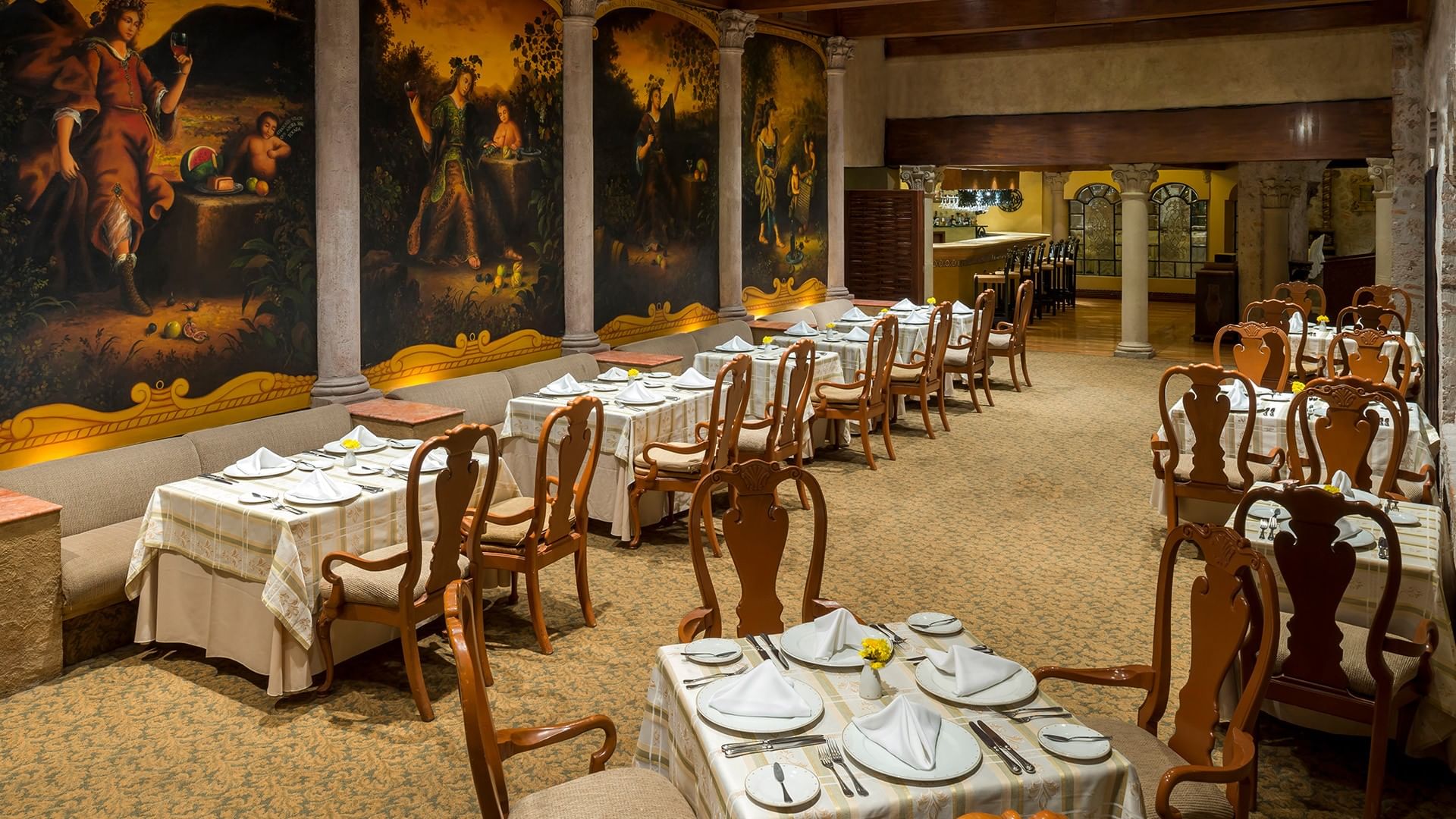 Elegant restaurant with white-clothed tables, wooden chairs, and historic murals on yellow walls at Quinta Real Aguascalientes