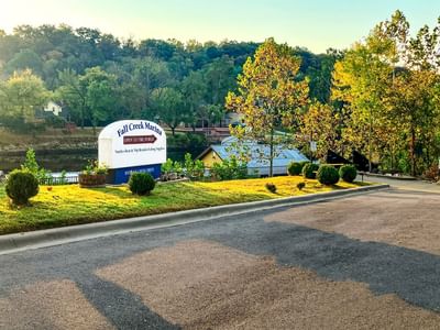 White and blue sign for Fall Creek Marina next to a body of water with trees in the background