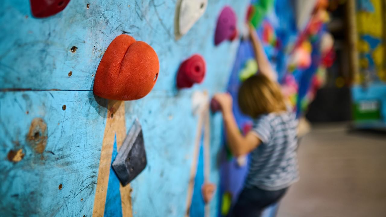 Colorful climbing wall with textured holds and a person reaching upward at Elevation Place.