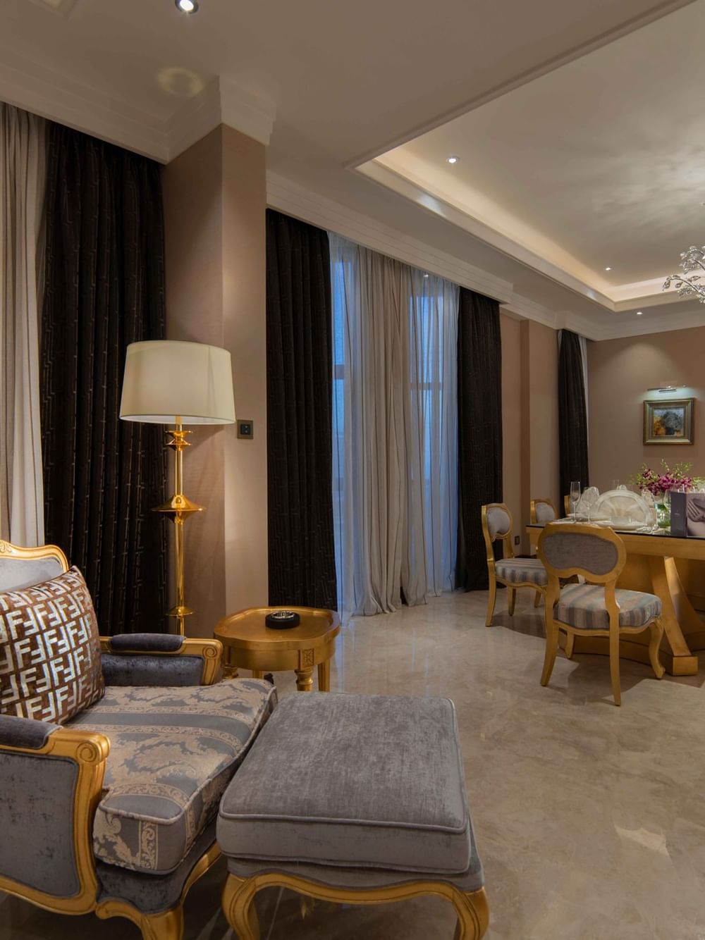 Gilded armchair & ottoman by a formal dining table under a massive crystal chandelier in Penthouse Villa at Warwick Al Khobar