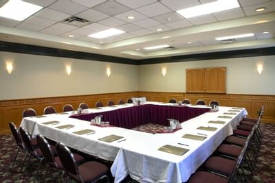 U-shaped conference table with maroon chairs by water glasses, under wall sconces at Glenmore Inn & Convention Centre