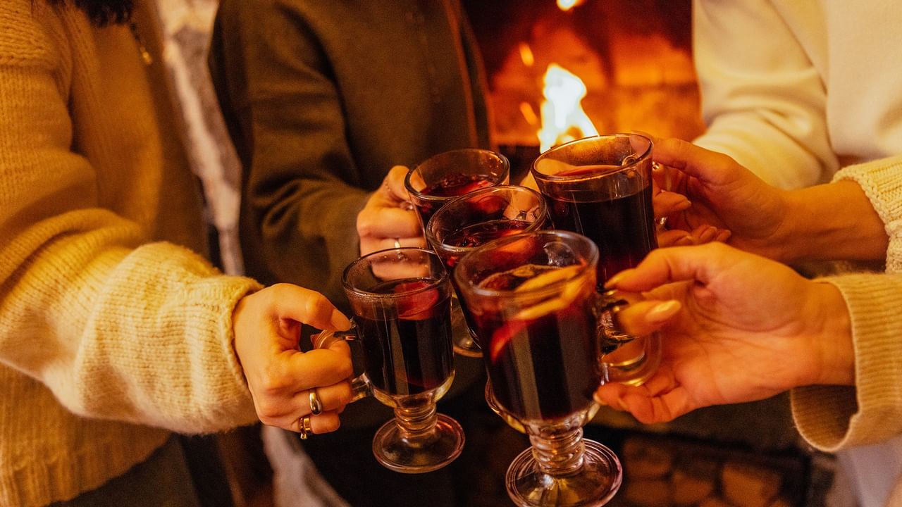 Friends toasting with mulled wine glasses by a glowing fireplace