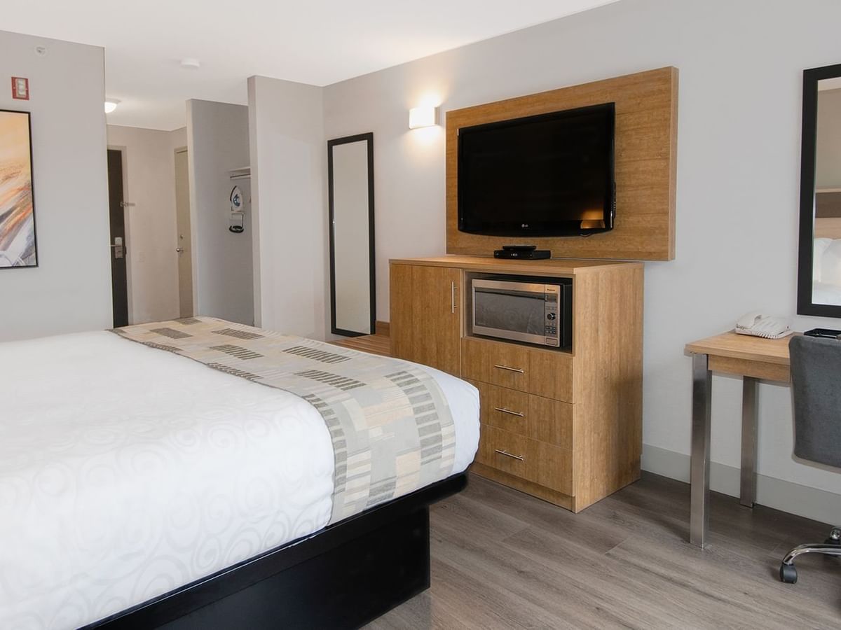 Hotel room with king bed, mirror, TV, microwave, chair, and desk