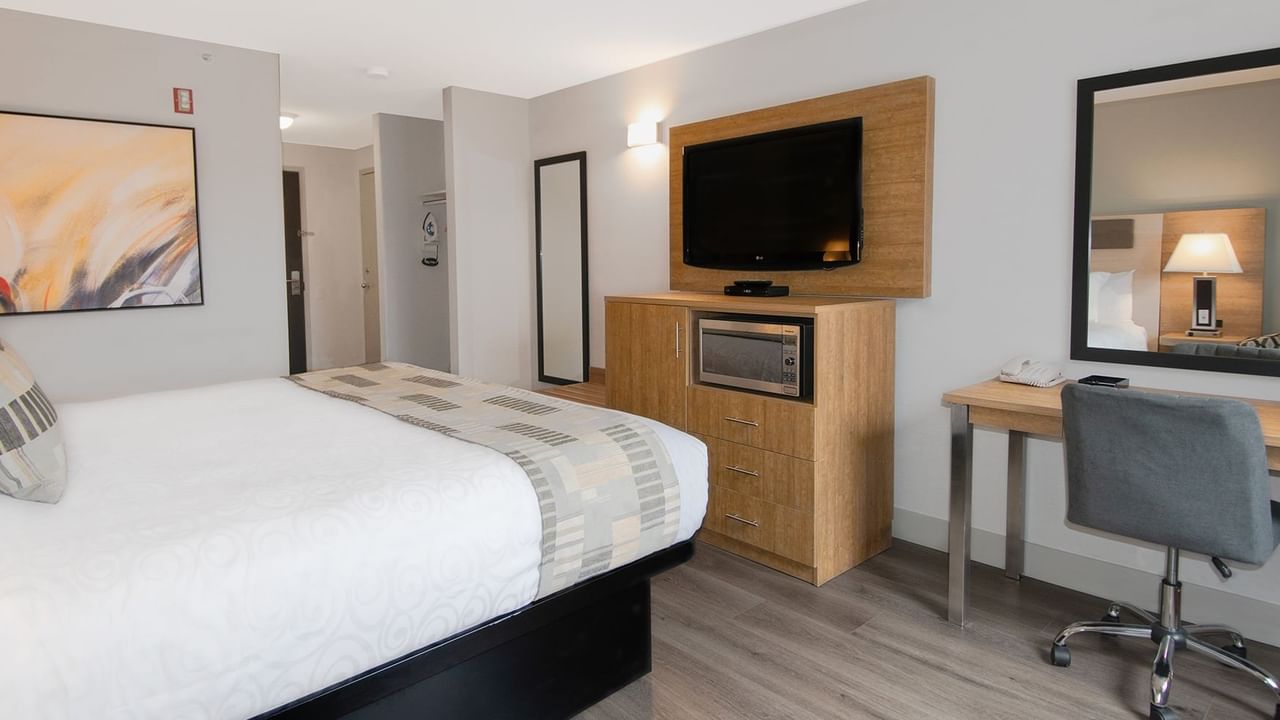 Hotel room with king bed, mirror, TV, microwave, chair, and desk