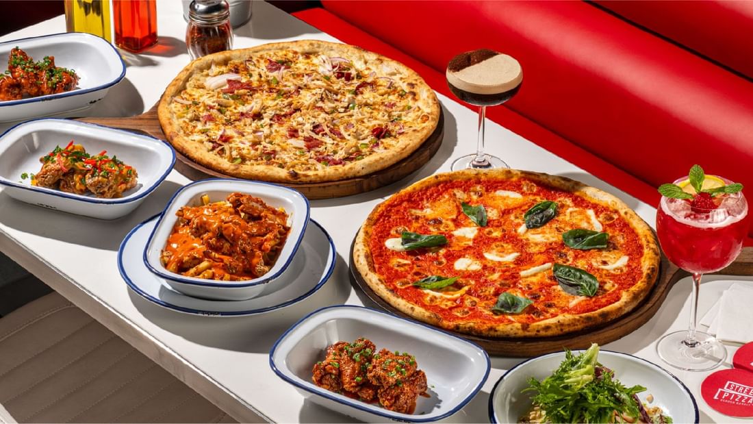 A vibrant table spread with two pizzas, chicken wings, and a cocktail at Sunway Lagoon Hotel