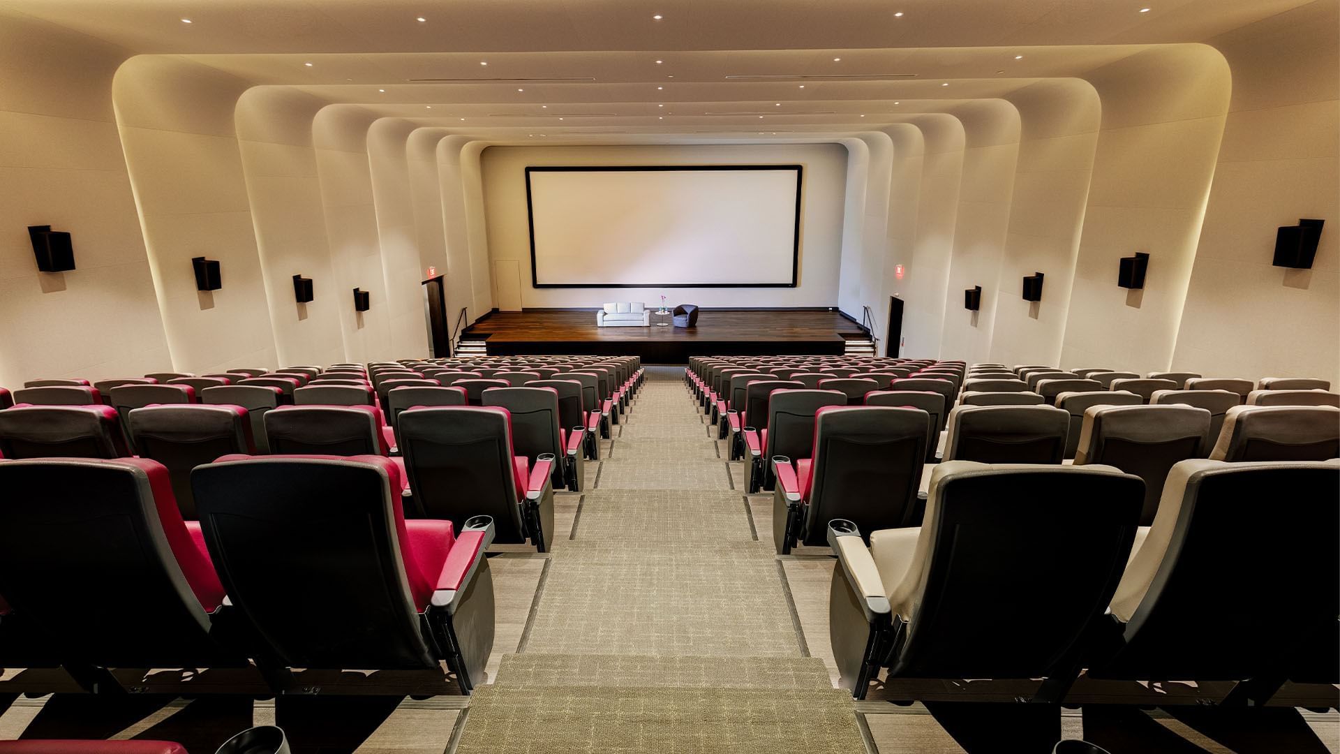 Modern screening room at Hotel X Toronto with red and grey seats and white couch on stage facing a large blank screen