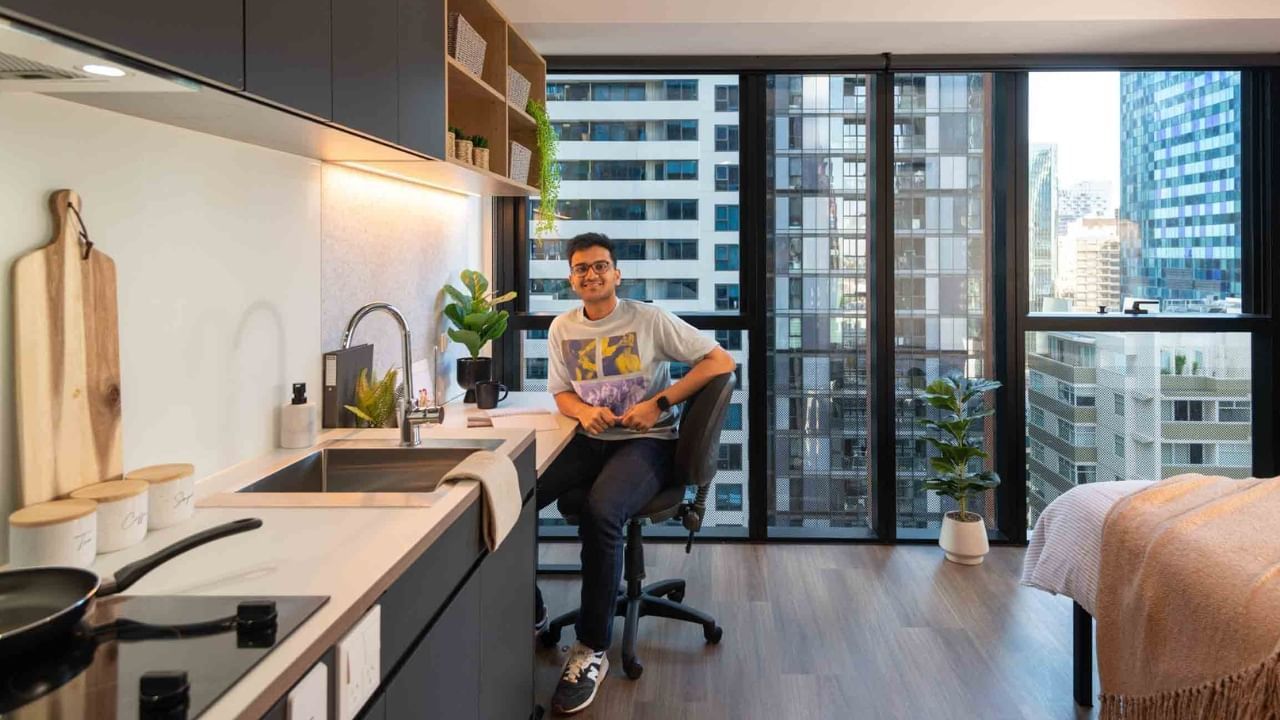 A resident sits at a kitchen counter in a modern studio apartment with city views.