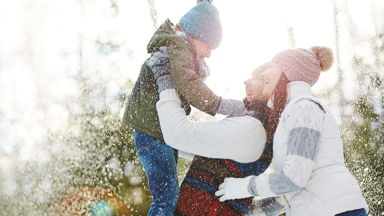 Mom holding child in arms in the snow with a friend