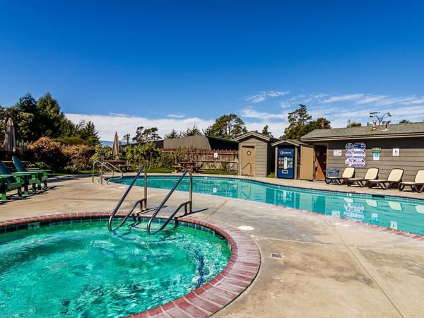 Outdoor pool area with a hot tub, lounge chairs, and a small building under a clear blue sky.