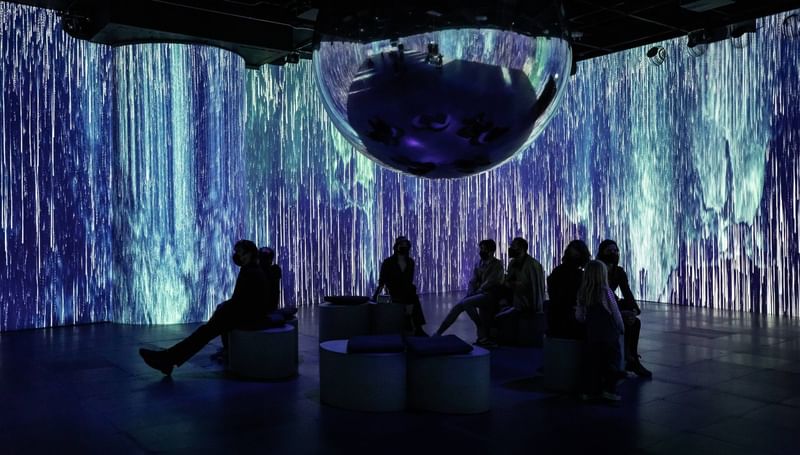 Guests relaxing on benches in an immersive digital art installation with blue projected light at Warwick Le Crystal Montreal
