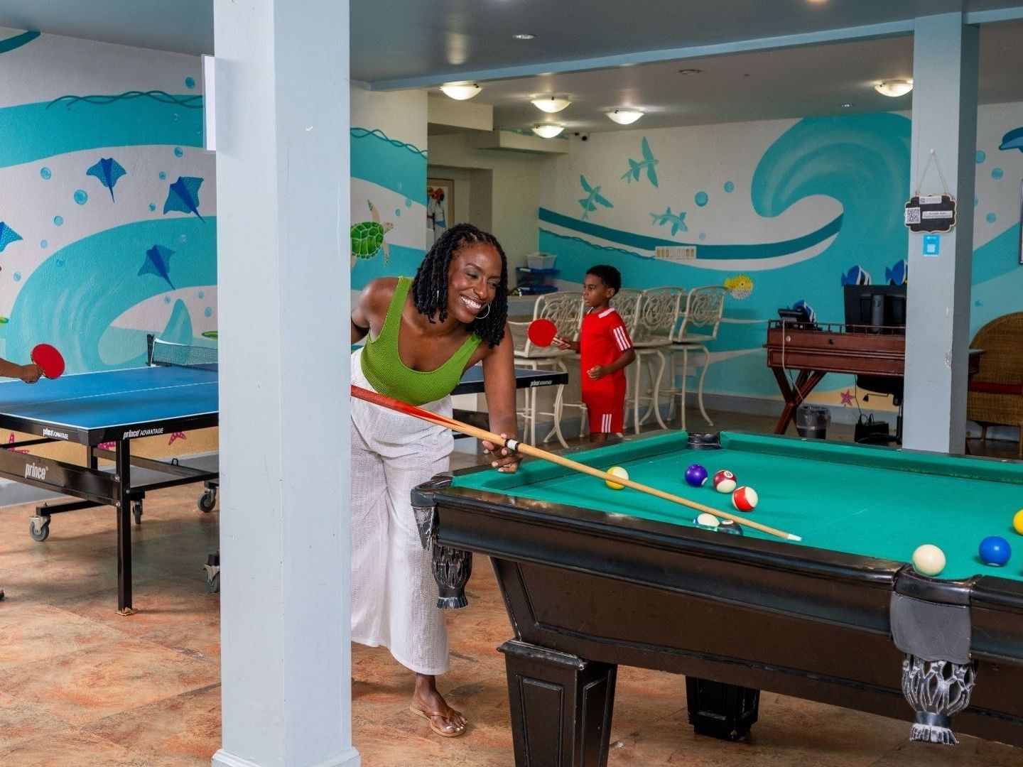 A woman and two children playing pool and ping pong in the game room at Savannah Beach Hotel.