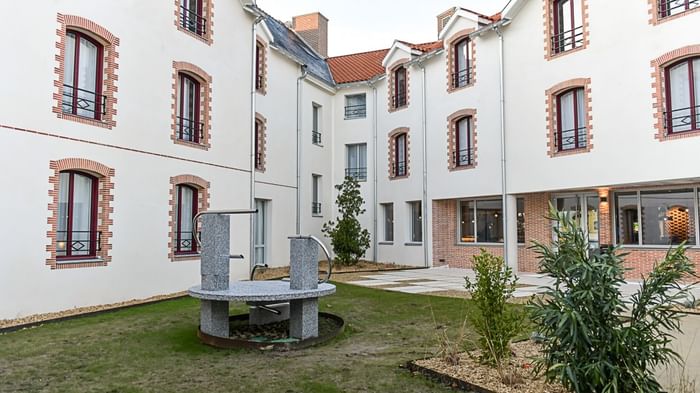 Vue extérieure de l'Hôtel Rivella avec cour, plantes et structure circulaire en pierre.