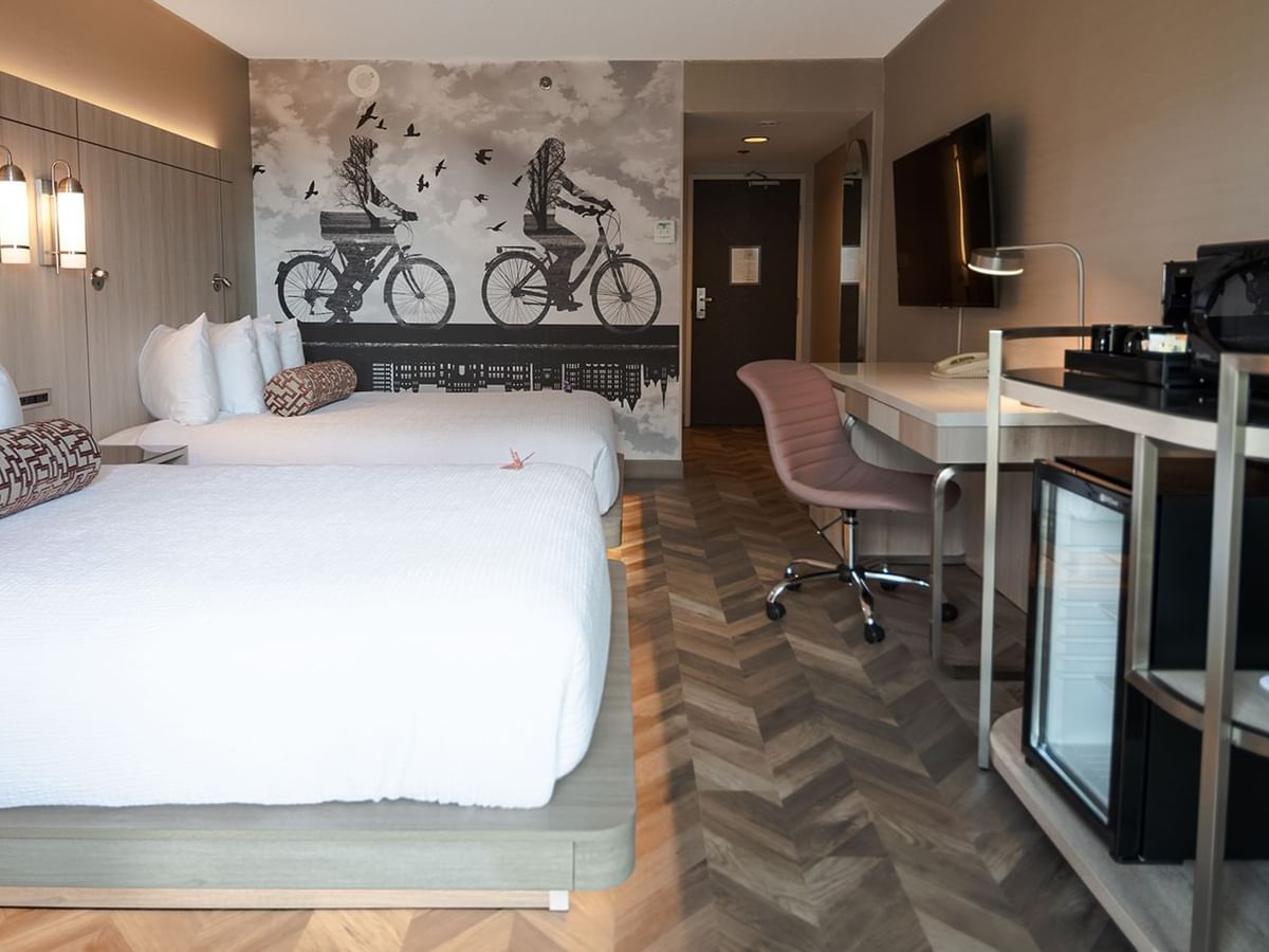 Hotel guestroom with two queen beds, mini fridge, microwave, TV, and work desk