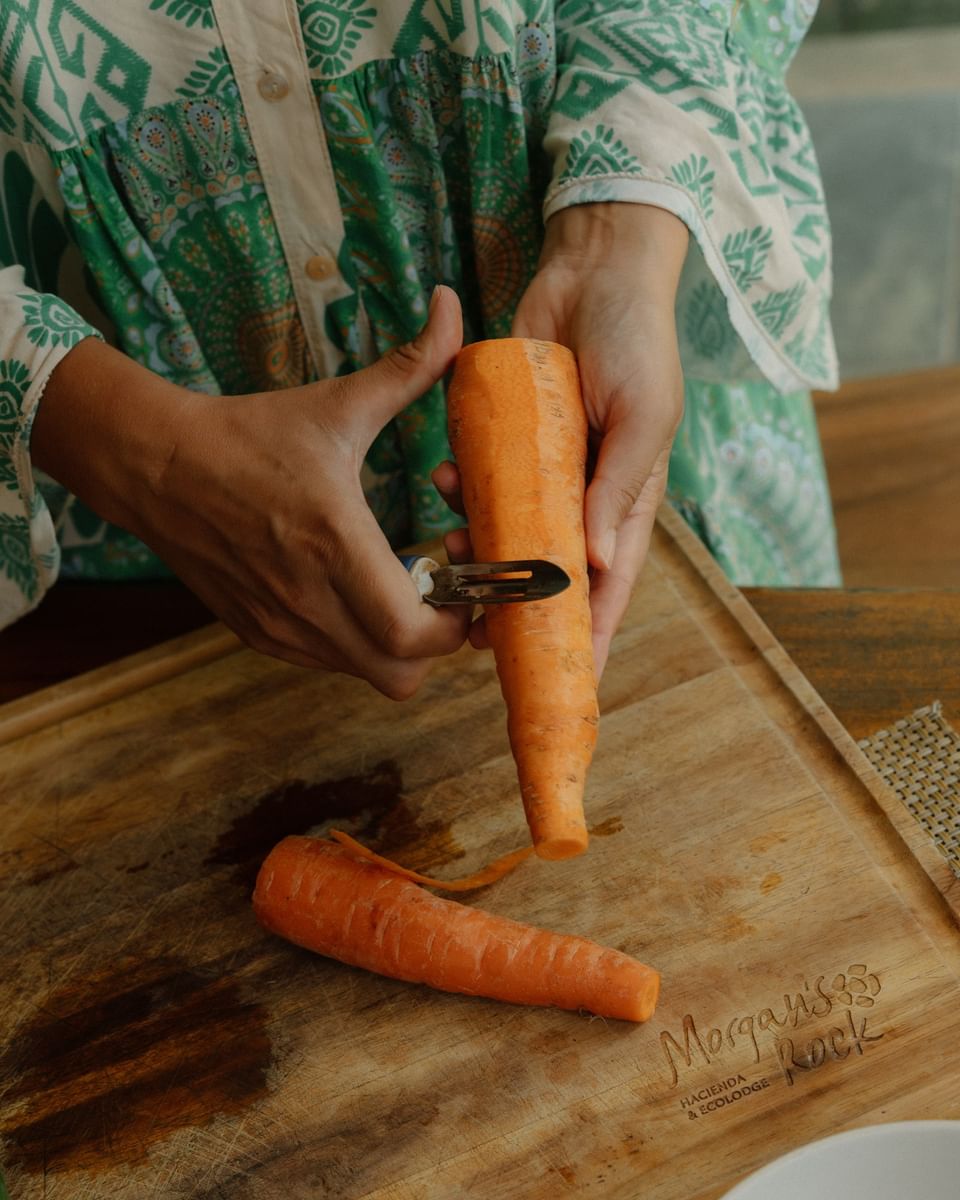 A woman peeling a carrot on a branded cutting board in La Bastide Restaurant kitchen at Morgan’s Rock Reserve & Ecolodge