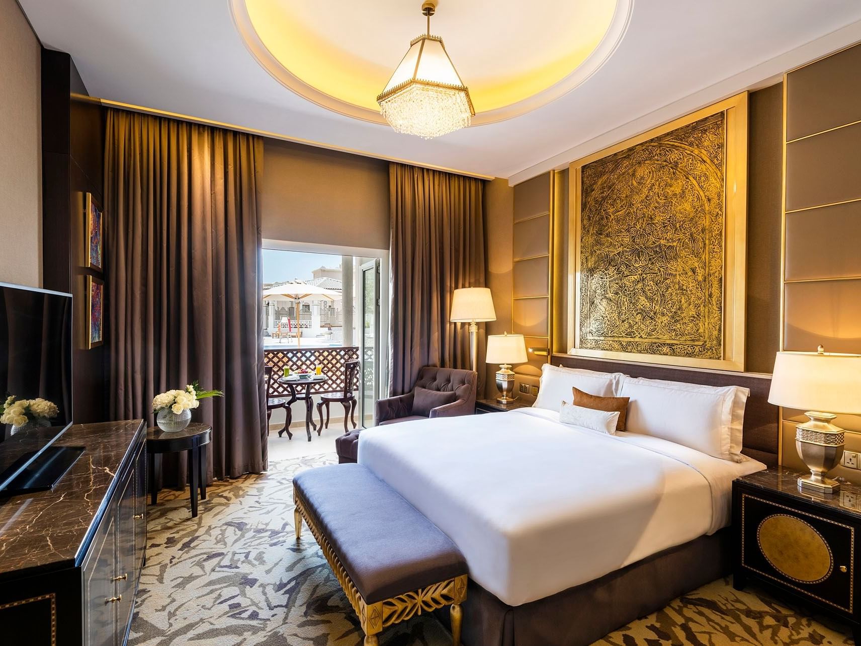 Luxurious hotel room with large bed, ornate decor, balcony, and elegant furniture.