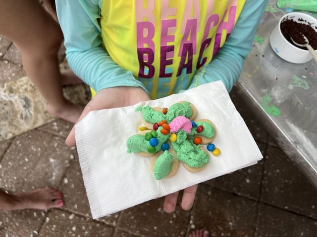 Child's hand holds a decorated cookie resembling a flower in a Cookie Decoration event at El Conquistador Resort