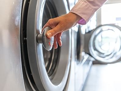 Person using a commercial washing machine at Coast Lonsdale Quay Hotel