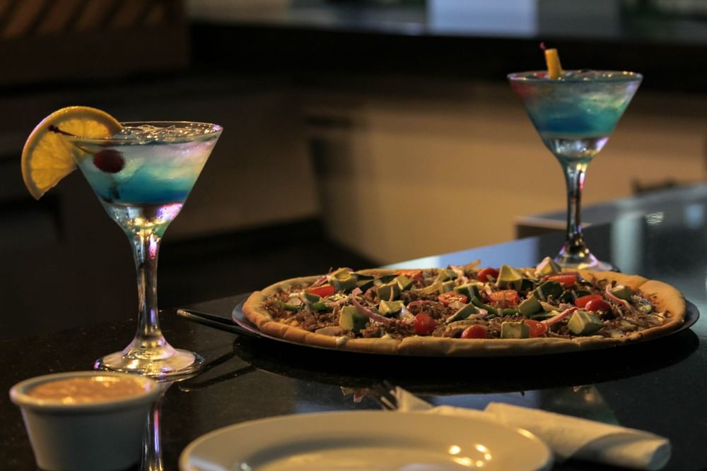 A gourmet pizza served with two vibrant blue cocktails in Solea Pizzería during a sunset dining session at Sunvivia Mazatlán