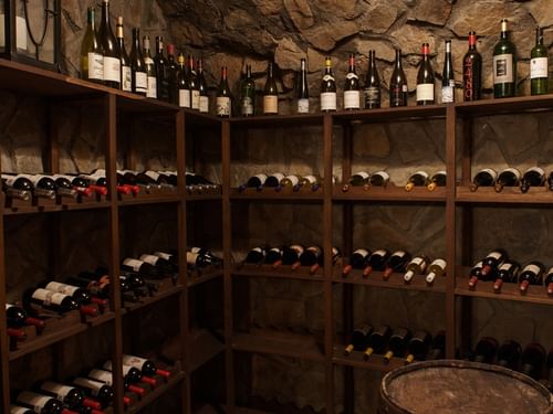 Cozy wine cellar with stone walls, a leather chair, and bottles of wine at La Cava de Santiago in Hacienda del Mar Los Cabos.