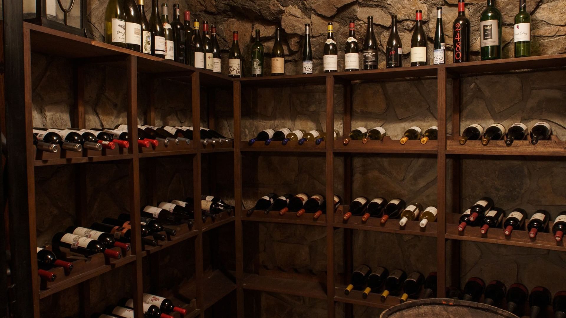 Cozy wine cellar with stone walls, a leather chair, and bottles of wine at La Cava de Santiago in Hacienda del Mar Los Cabos.