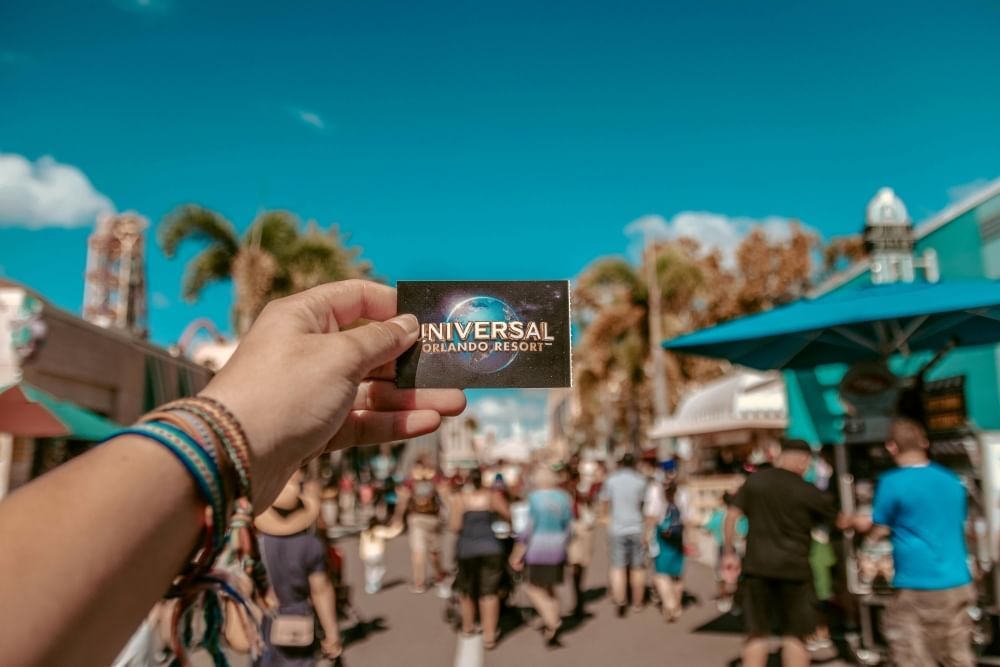 A hand holds a Universal Orlando Resort ticket in front of shops at CityWalk.