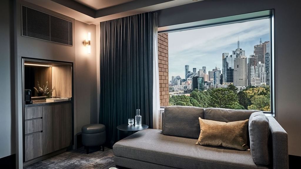 Modern suite with gray sofa, city skyline views at Pullman East Melbourne
