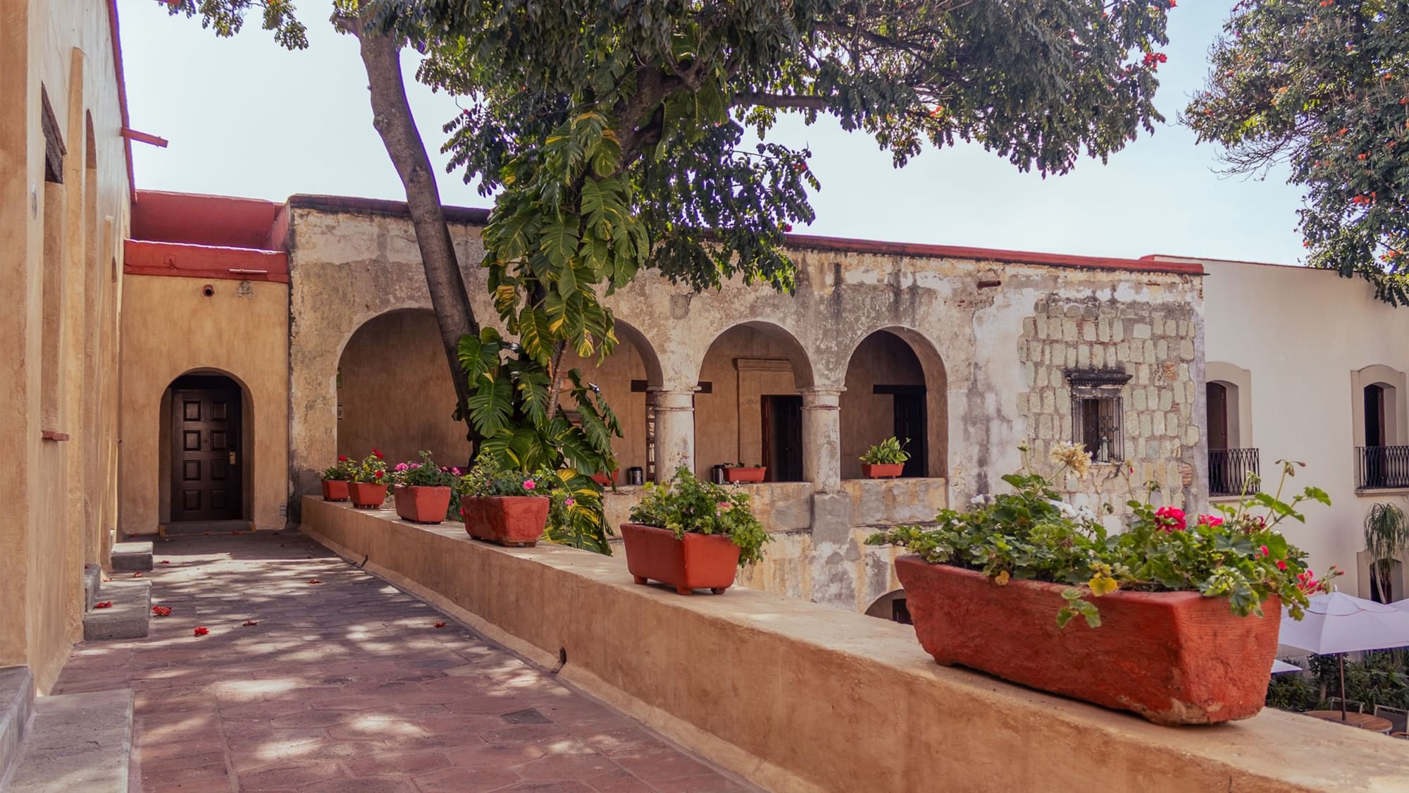 Corredor histórico del hotel con arcos de piedra y macetas rojas en una repisa en Quinta Real Oaxaca