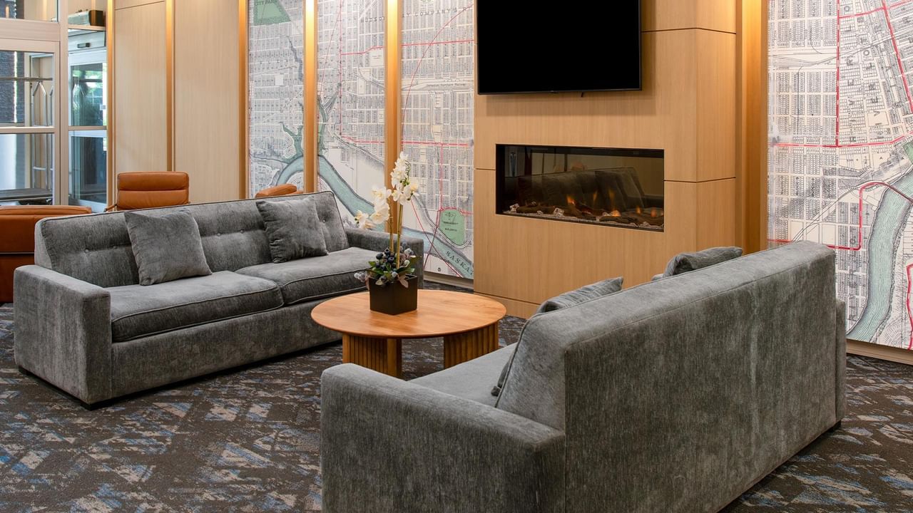 Hotel lobby lounge with sofas, armchairs, a fireplace and wall-mounted TV.