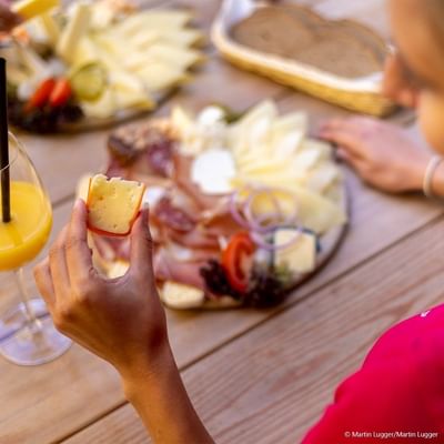 Woman holding a cheese slice in front of a cheese platter and a glass of orange juice.