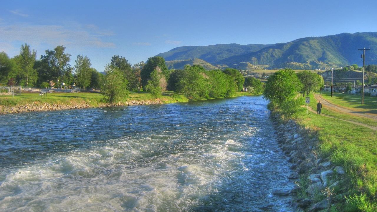 A lazy river with white water rapids, trees, and mountains in the background in Penticton, B.C