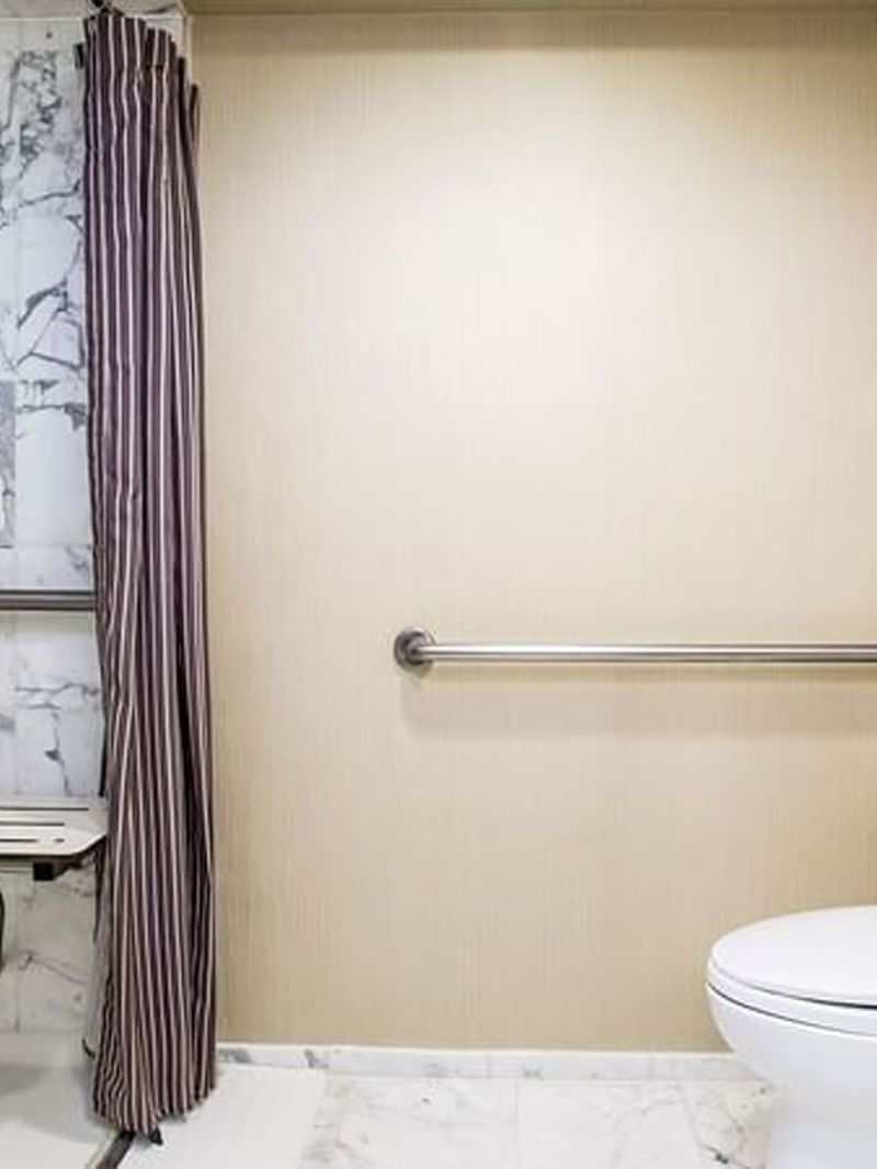 Handicap accessible bathroom featuring a white toilet and shower seat in Accessible Deluxe Rooms at Warwick Seattle