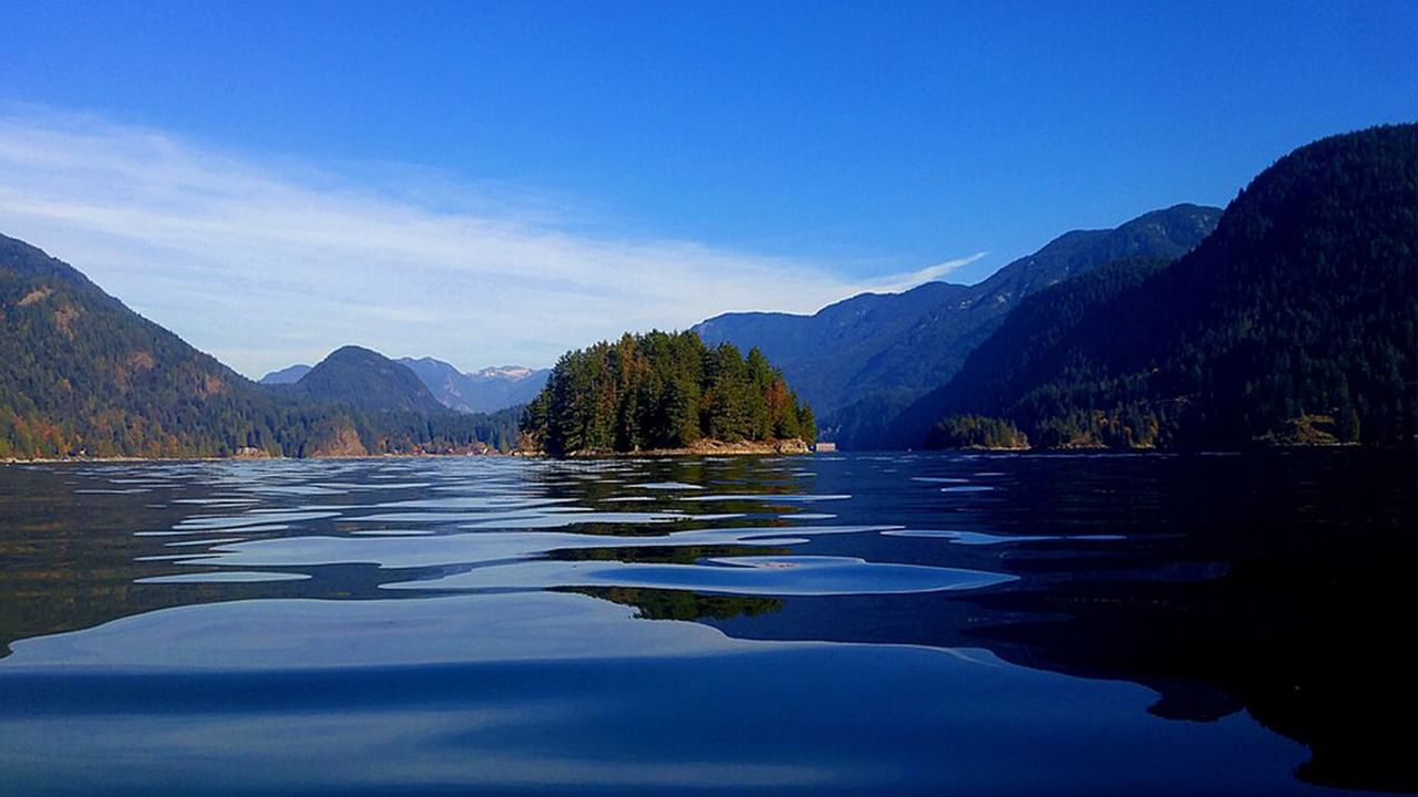 Lake with clear blue water reflects the sky and mountains under a partly cloudy blue sky near Coast Lonsdale Quay Hotel