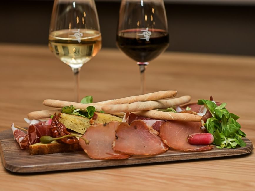 Deux verres de vin et assiette de charcuterie sur planche en bois au Hôtel Rivella.