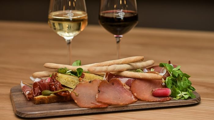 Deux verres de vin et assiette de charcuterie sur planche en bois au Hôtel Rivella.